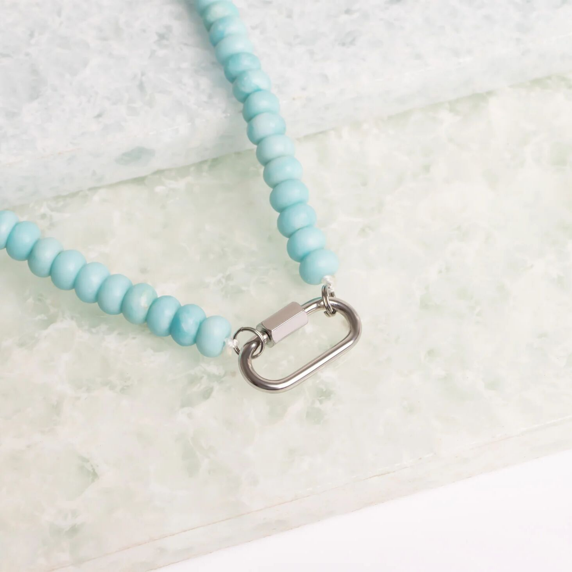 Detail of silver stainless steel carabiner clasp on blue beaded necklace