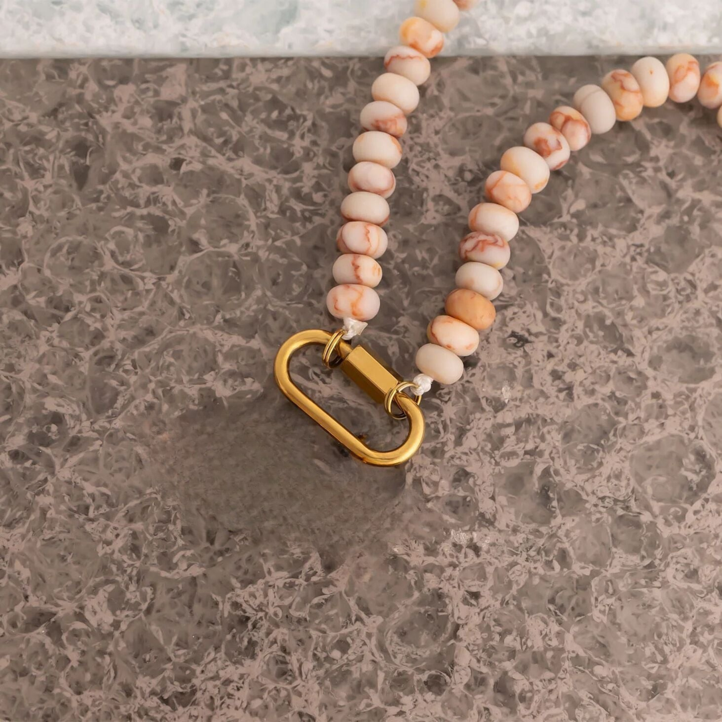 Blush marble stone necklace with 18K gold stainless steel clasp on marble surface